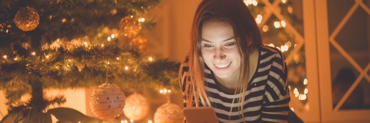 Female laying down next to christmas tree looking at phone_shutterstock_650929771-min